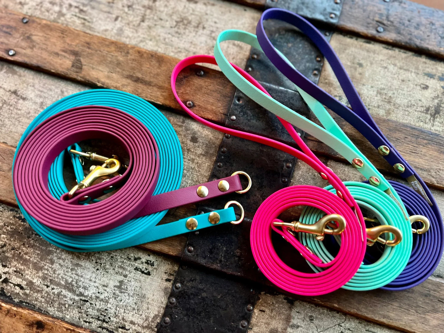 Colorful Your Whole Dog Trailblazing Tails: Long Line and Leash Extension (1/2 inch/Medium Dog) in pink, teal, purple, and black are arranged on a wooden and metal surface, showcasing both durable dog leash options and waterproof designs.