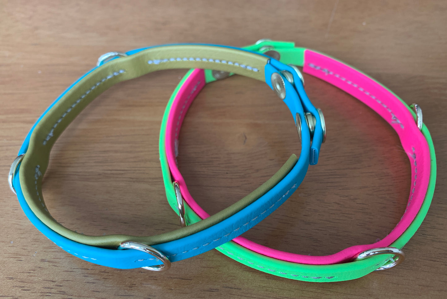 Two brightly colored, handcrafted dog collars, one blue and green and the other pink and green, are placed on a wooden surface. Their durable design complements Trailblazing Tails: The Leash Organiser by Your Whole Dog beautifully.