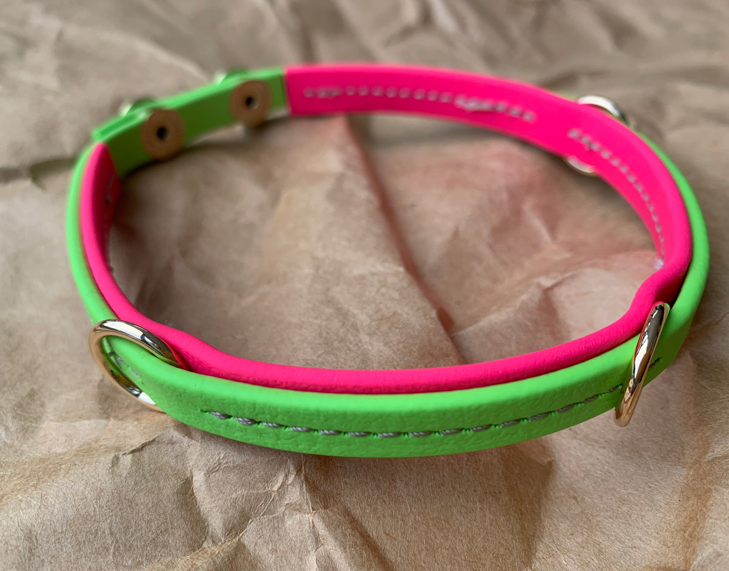 A close-up of Your Whole Dog's Trailblazing Tails: The Leash Organiser, a handcrafted vibrant green and pink collar with silver rings, laid on a crinkled beige surface.