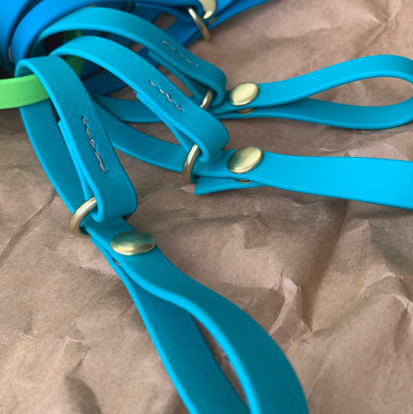 Close-up of blue leather straps with brass hardware, arranged on crumpled brown paper, perfect to cinch your Trailblazing Tails: The Long Line Holder or attach to belt by Your Whole Dog.