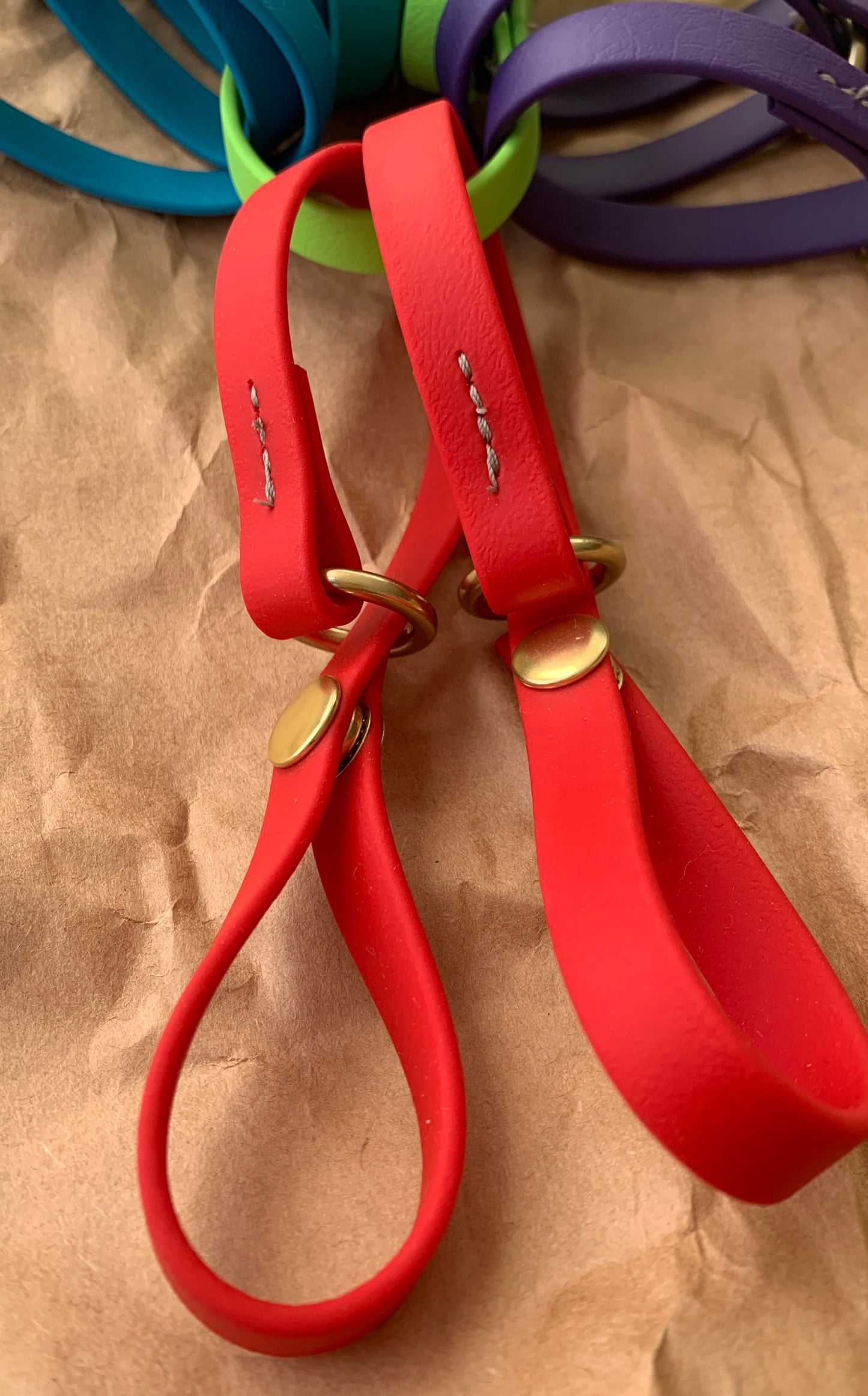 Close-up of red leather loops with brass hardware, perfect to attach to a belt, against a brown background. Introducing Trailblazing Tails: The Long Line Holder by Your Whole Dog.