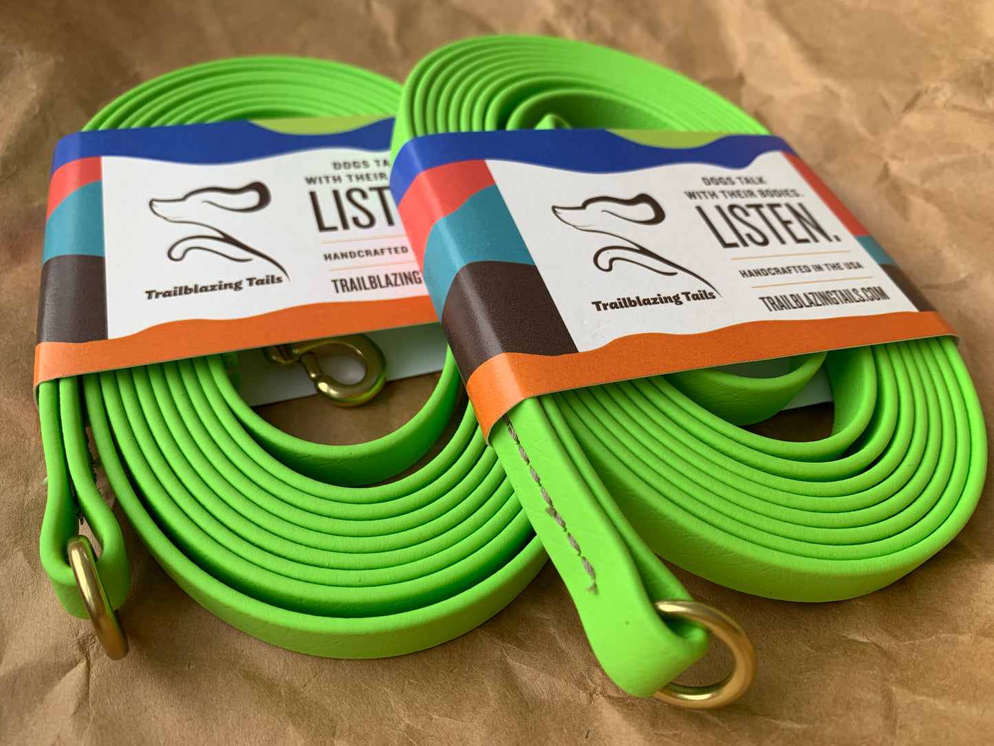 Two durable, neon green dog leashes with brass hardware are coiled and labeled with "Trailblazing Tails: Long Line and Leash Extension (1/2 inch/Medium Dog)" branding by Your Whole Dog, placed on a brown paper background.