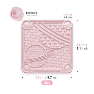 The PAW Planet Lick Pad by Your Whole Dog is a pink silicone square baby plate with a raised planet design and suction cups in the top left. It measures 23 cm x 22 cm (9.1 x 8.7 inches) with a suction cup diameter of 3.5 cm (1.4 inches), ideal for slow feeding.