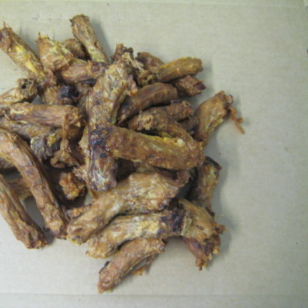 A pile of Superior Pet Food Co. (Ranchmans) Chicken Necks lies on a beige background, providing an easily digestible treat for pets.