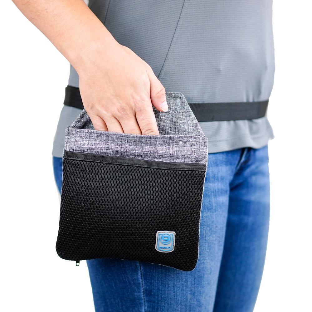 A person uses the Blue-9 INSPIRE Training Treat Pouch, placing their hand inside its black mesh pouch with a gray flap—perfect for training treats. Dressed in a gray shirt and blue jeans, they blend practicality and style.