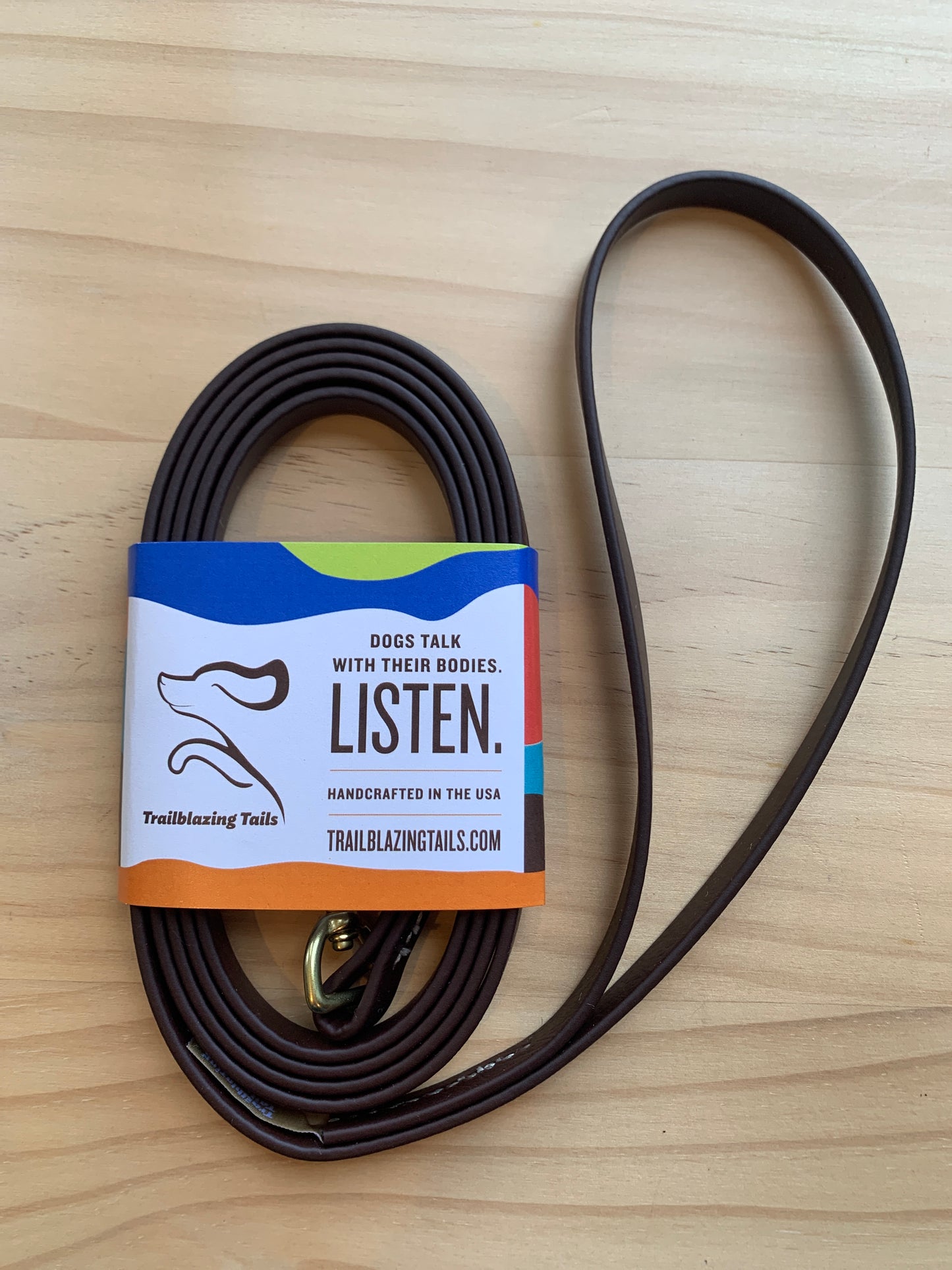 A rolled-up brown, ultra-lightweight leash with a label that reads "Dogs talk with their bodies. Listen." and "Trailblazing Tails: The Little Dog." The label also mentions it is handcrafted in the USA by Your Whole Dog.