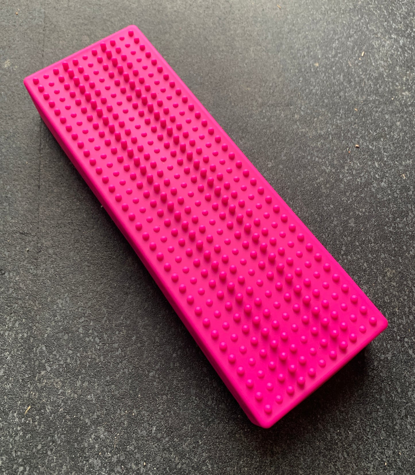 Rectangular pink Flexiness StackingBar by Flexiness Canine Fitness Equipment, featuring small raised bumps on a dark gray surface, offers SensiMat compatibility for enhanced versatility.