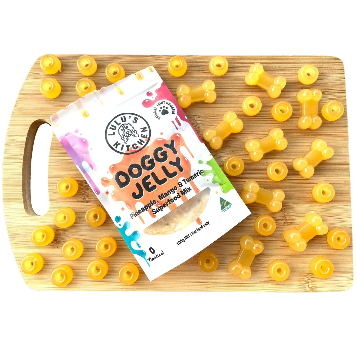 On a cutting board rests a package labeled "Lulu's Kitchen Doggy Jelly - Pineapple, Mango & Tumeric," surrounded by bone-shaped orange jellies.