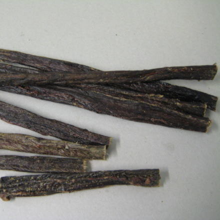 On a light surface, several dark, dried root sticks resemble our Superior Pet Food Co. Ranchmans Beef Chewy Sticks—100% natural pet treats with no additives.