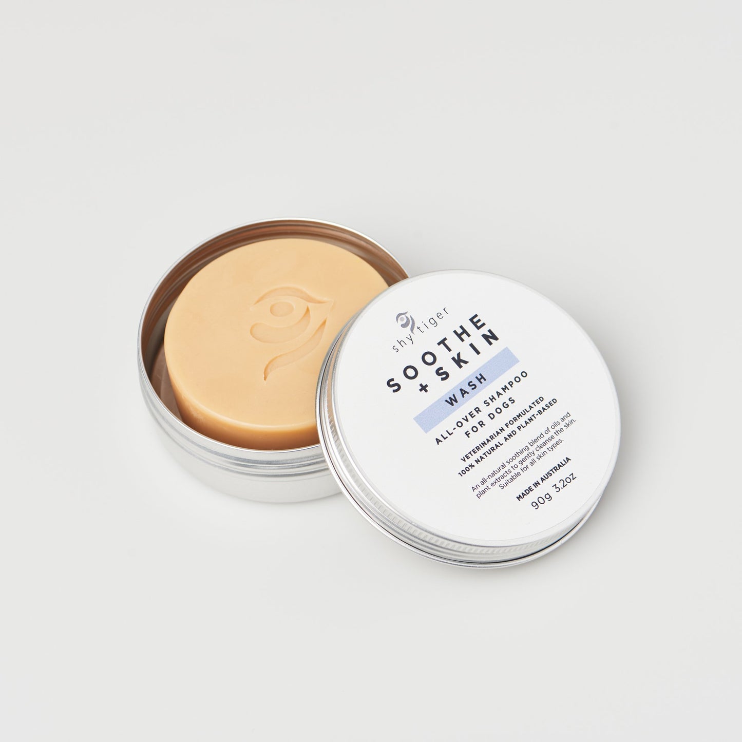 Circular solid shampoo bar for dogs formulated by veterinarians, packaged in a tin featuring a white label with "Soothe & Skin Wash." This all-natural bar is 90g and includes an embossed logo, making it an eco-friendly grooming solution for your pet from the brand Your Whole Dog's Shy Tiger line.