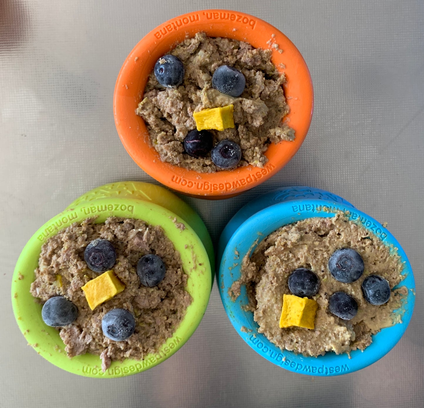 A collection of three stuffed West Paw Toppls at Your Whole Dog. They are topped with blueberries and a cube of goat's cheese.