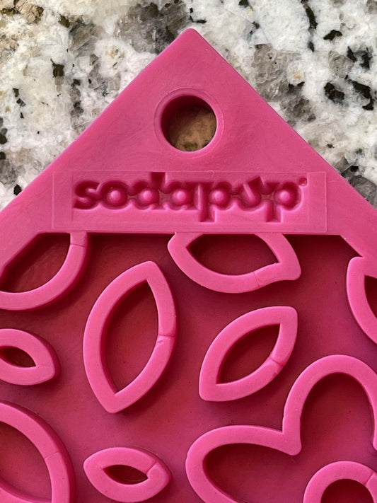 Close-up of a pink 'Soda Pup' branded dog enrichment toy with a honeycomb pattern designed for licking.