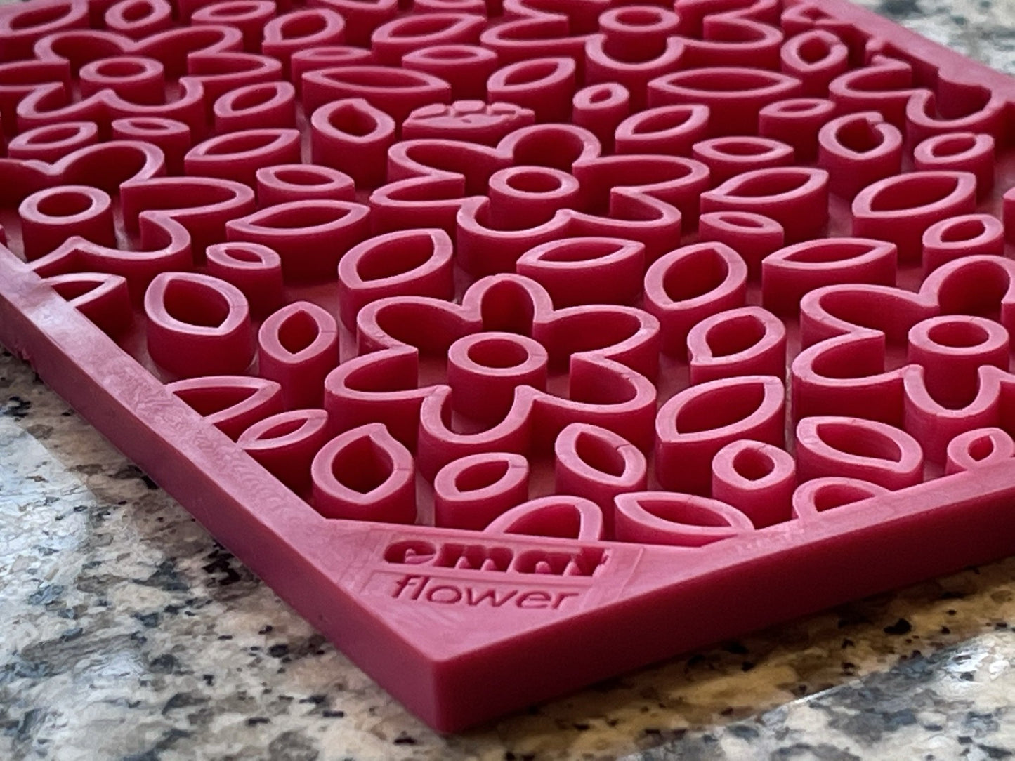 Close-up of the Soda Pup EMAT Enrichment Licking Mat in pink silicone, featuring floral and leaf cutouts on a speckled gray surface, ideal for engaging dog foraging activities.