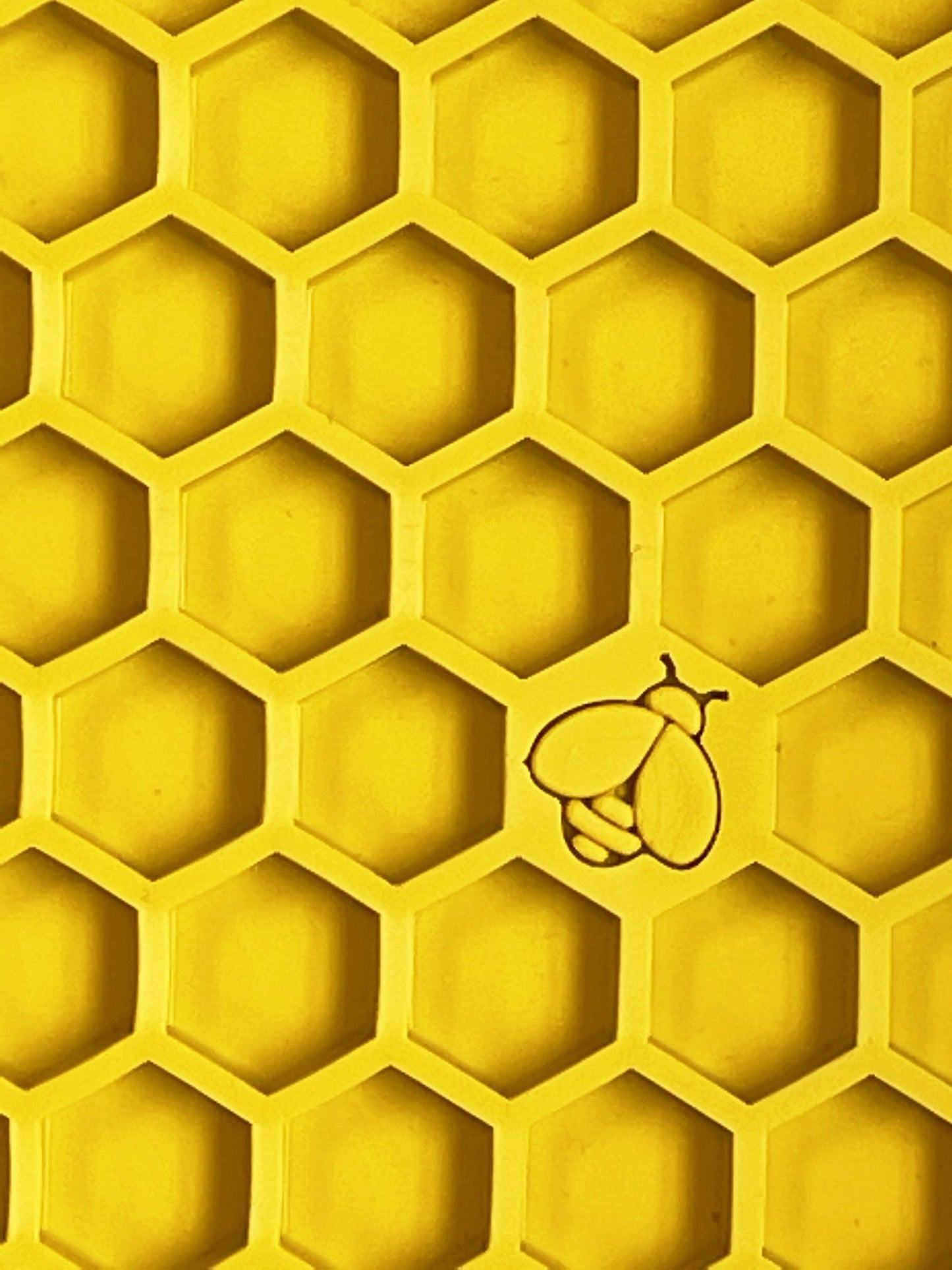 A close-up of a yellow honeycomb pattern with one cell containing a small bee, designed to mimic Your Whole Dog's Soda Pup EMAT ENRICHMENT LICKING MAT.