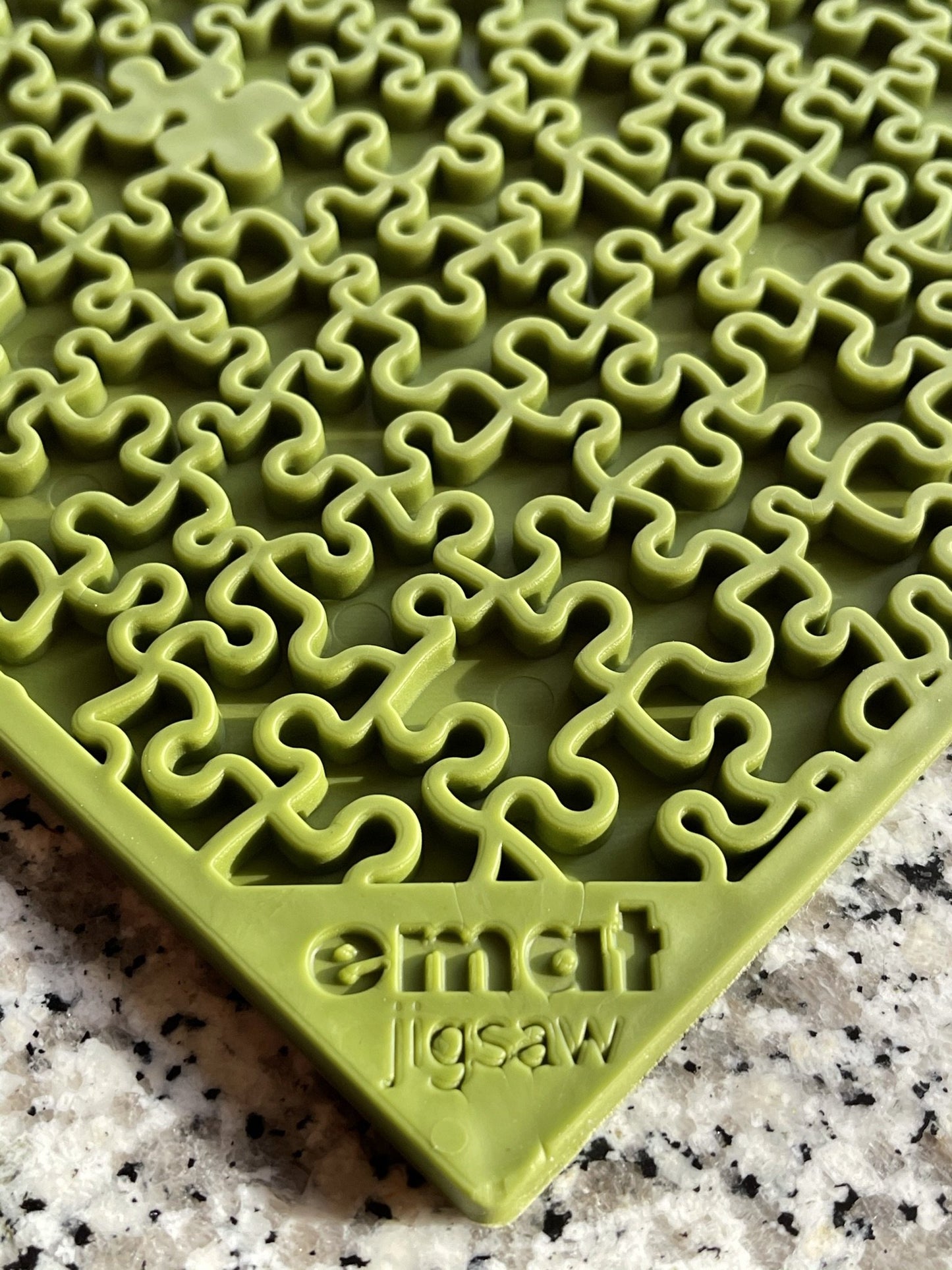 Close-up of a green Soda Pup EMAT Enrichment Licking Mat with interlocking pieces on a speckled surface. The text "emat jigsaw" is embossed in one corner, ideal for dog foraging activities to keep your pet engaged and mentally stimulated.