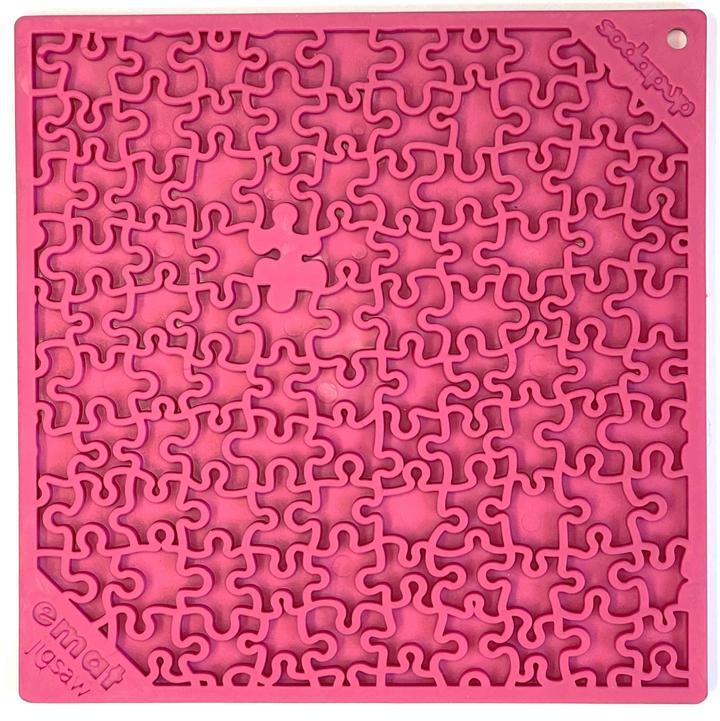 The CLEARANCE: Soda Pup EMAT ENRICHMENT LICKING MAT by Soda Pup is a pink, silicone mat with a jigsaw design featuring a missing piece in the center. It's perfect for dog foraging activities, providing an engaging and stimulating puzzle to keep your furry friend entertained.