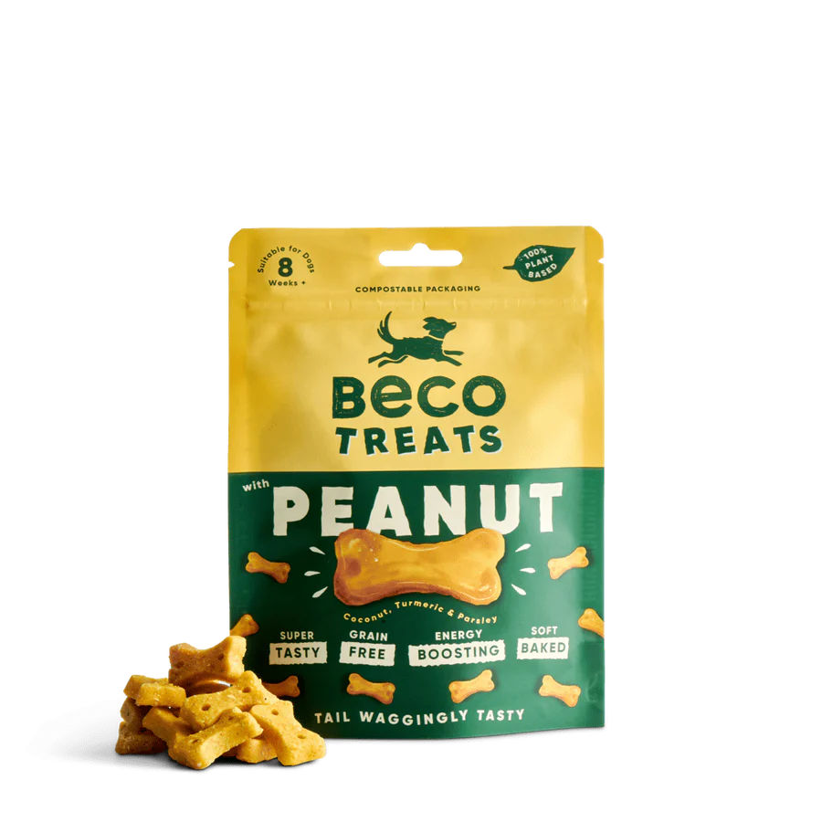 A pack of Beco Pets Peanut Dog Treats with Coconut & Turmeric stands upright, with bone-shaped treats in front. The Beco packaging highlights features like grain-free and energy boosting.