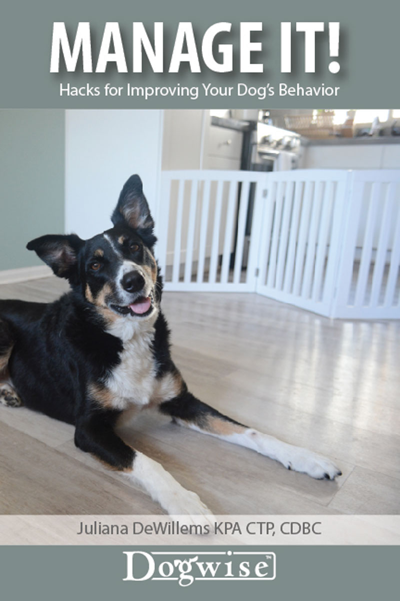 A black and tan dog lies on a wooden floor in front of a white gate; text reads "Book: Manage It! Hacks for Improving Your Dog’s Behavior" by Juliana De Willems, from Your Whole Dog.