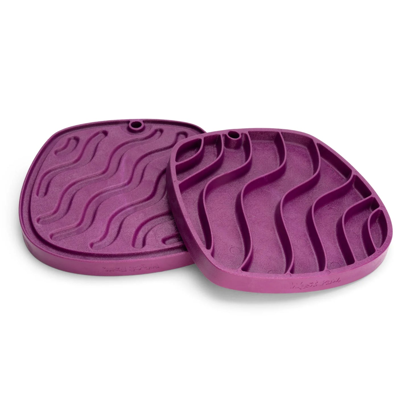 Two West Paw Feast Mats from Your Whole Dog, crafted from recycled ocean-bound plastic and featuring a wavy pattern in purple, are displayed. One mat is laid flat while the other is propped against it.