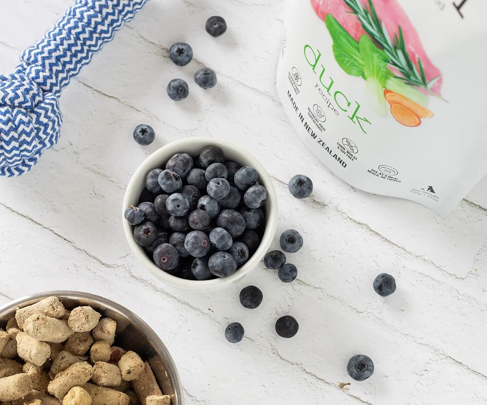 A bowl of delicious blueberries next to a bag of Woof: Freeze Dried Duck Dog Food from Your Whole Dog.
