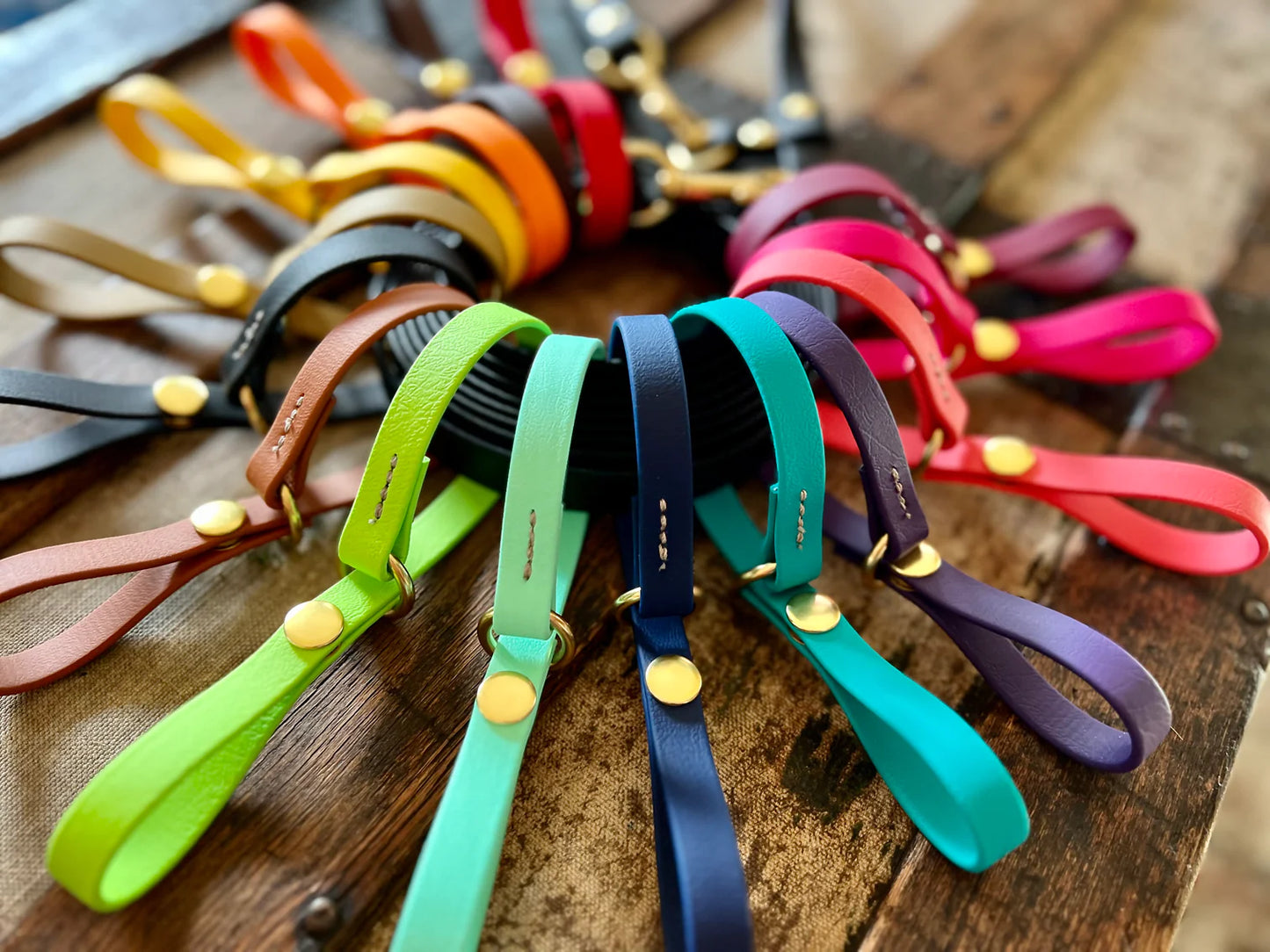 A group of colorful Trailblazing Tails: The Long Line Holder leashes, featuring snap closures, arranged on a wooden table.