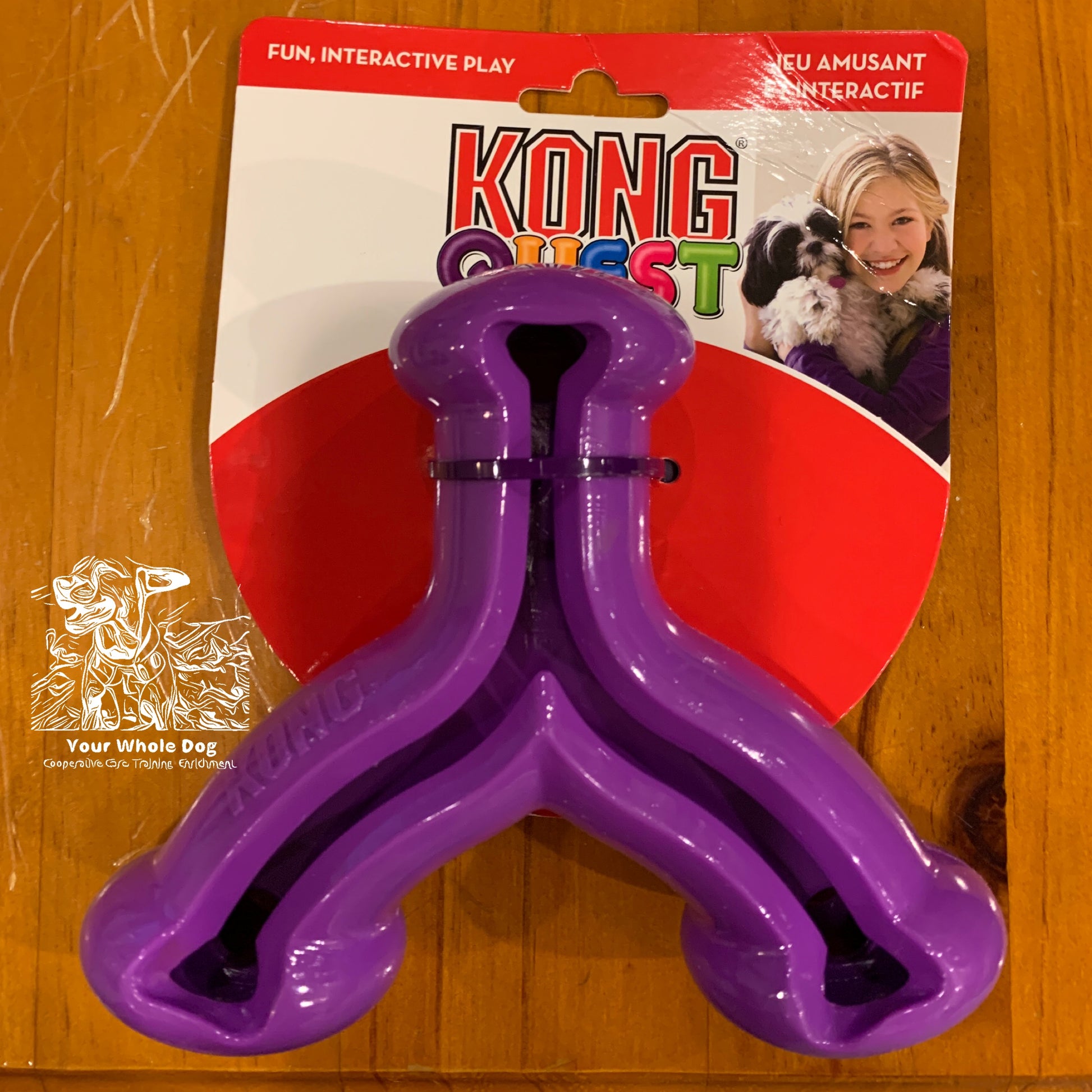 A packaged purple KONG Quest Wishbone treat-dispensing toy by Your Whole Dog, featuring a photo of a woman smiling while holding a dog. The packaging highlights its ability to provide fun, interactive play that promotes natural foraging behaviors.